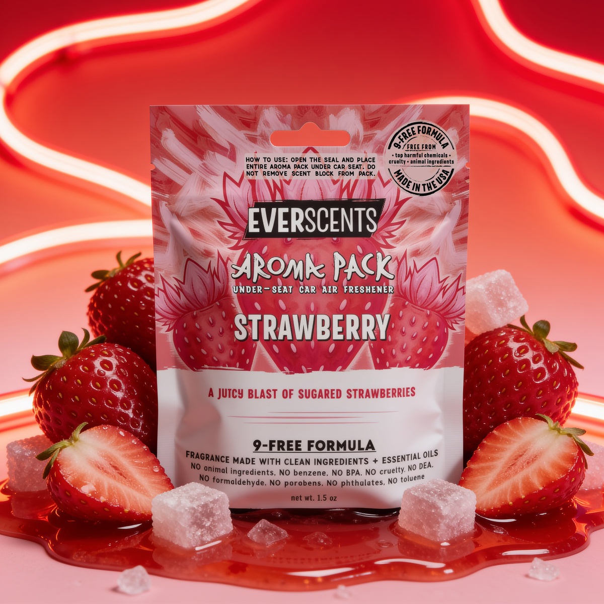 A front-facing scene of an Everscents Aroma Pack under-seat car air freshener pouch in the Strawberry scent sitting upright and artfully surrounded by whole and sliced fresh red strawberries and sugar cubes sitting in a small puddle of red jelly. The scene is vibrant and fun, accented by wavy glowing neon red light tubes trailing across a seamless red and pink gradient studio background.