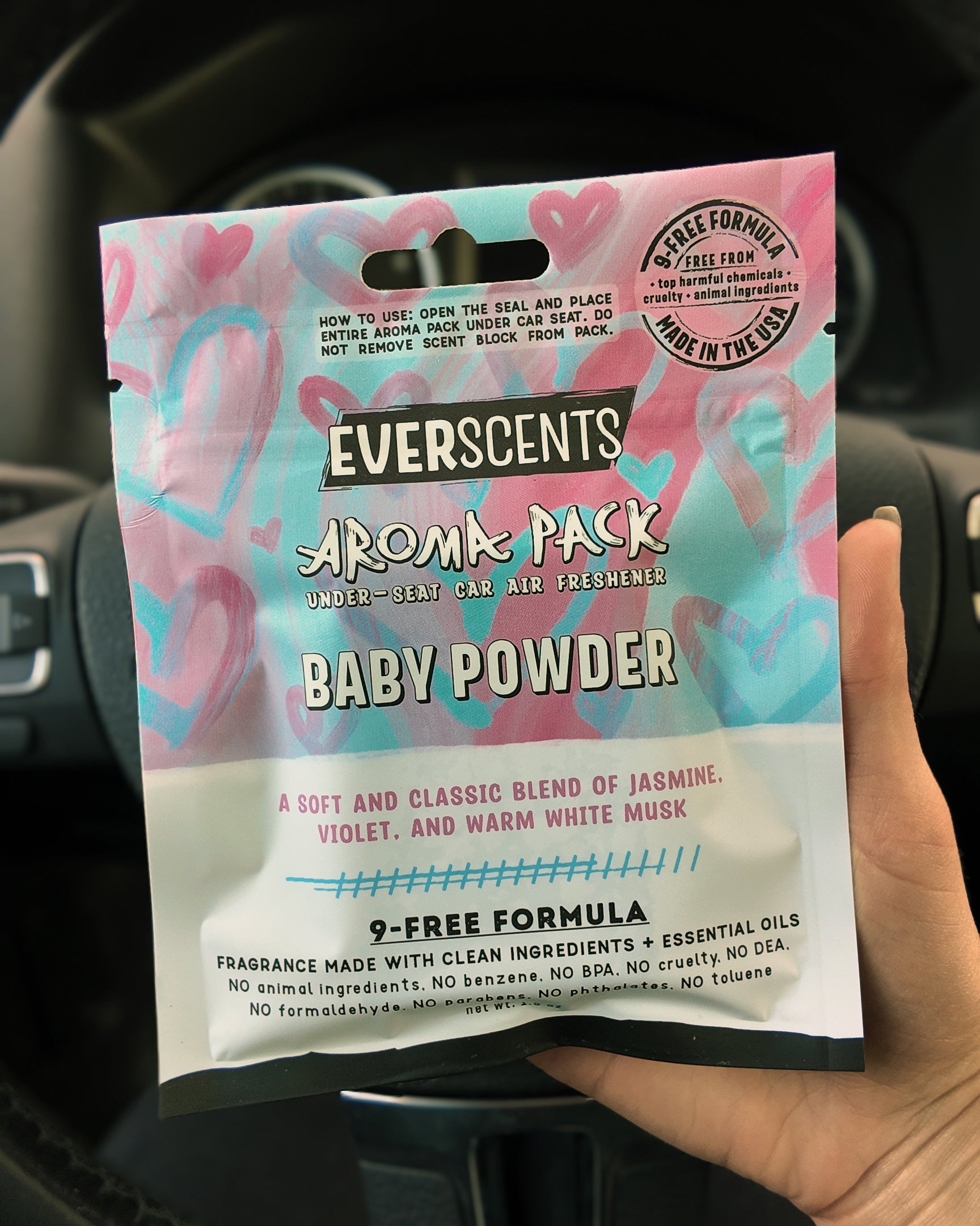 Everscents Aroma Pack Baby Powder air freshener held in front of a car interior steering wheel