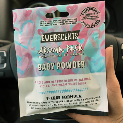 Everscents Aroma Pack in the scent Baby Powder held in front of a black car dashboard. The pouch is large, covering the hand holding it.
