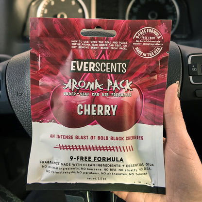 Everscents Aroma Pack in the scent Cherry held in front of a black car dashboard. The pouch is large, covering the hand holding it.