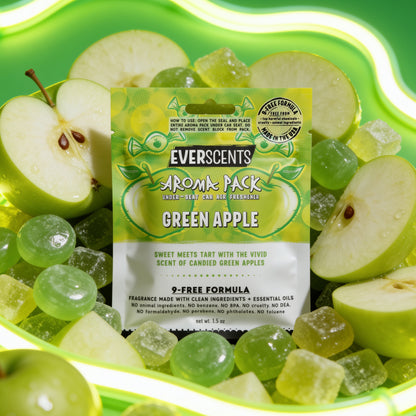 A front-facing scene of an Everscents Aroma Pack under-seat car air freshener pouch in the Green Apple scent sitting upright and artfully surrounded by apple slices and green apple candies. The scene is vibrant and fun, accented by wavy glowing neon green light tubes trailing across a bright green studio background. The scene evokes a high-end fun and fruity atmosphere.